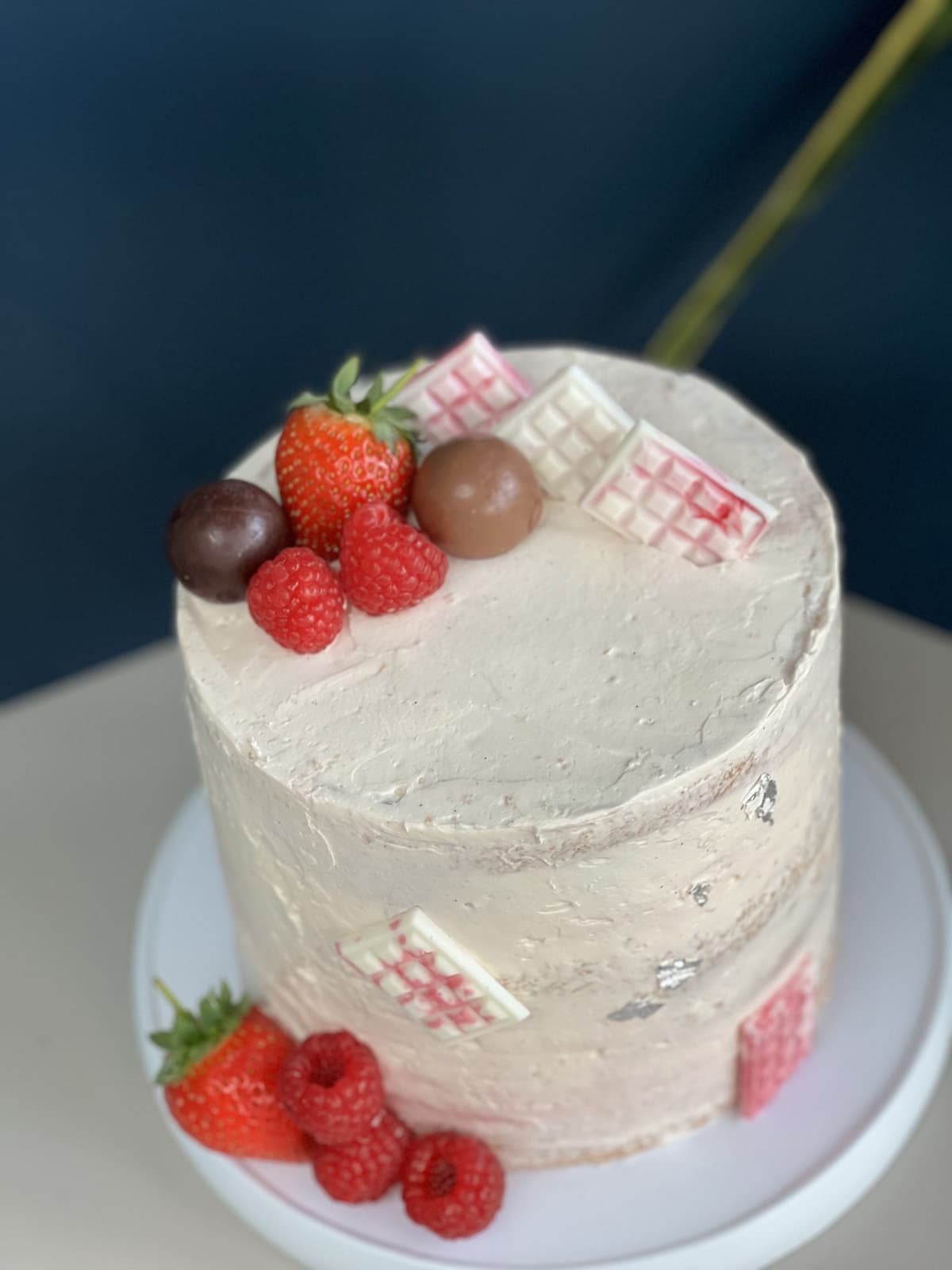 White buttercream cake topped with strawberries, raspberries and pink chocolate squares