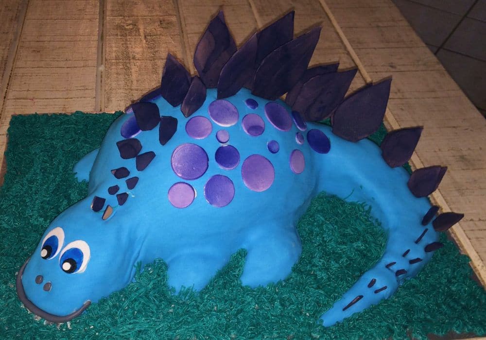 Blue and purple stegosaurus cake on green buttercream grass