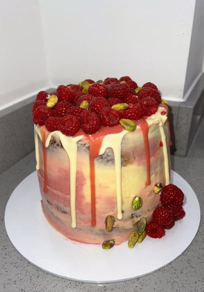 Raspberry and pistachio drip cake topped with fresh raspberries