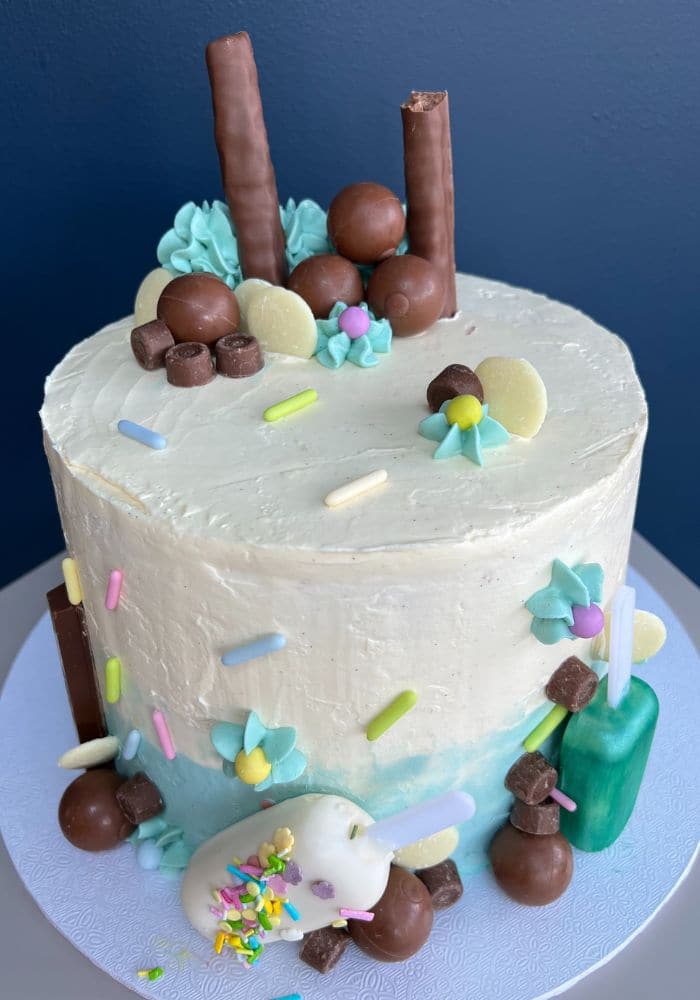 White buttercream cake with sprinkles, chocolate balls and pastel sugar flowers