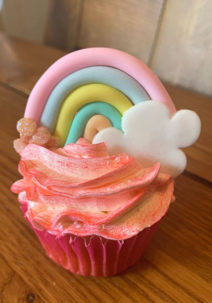 Cupcake with pink ruffled frosting topped with a pastel sugar rainbow and cloud