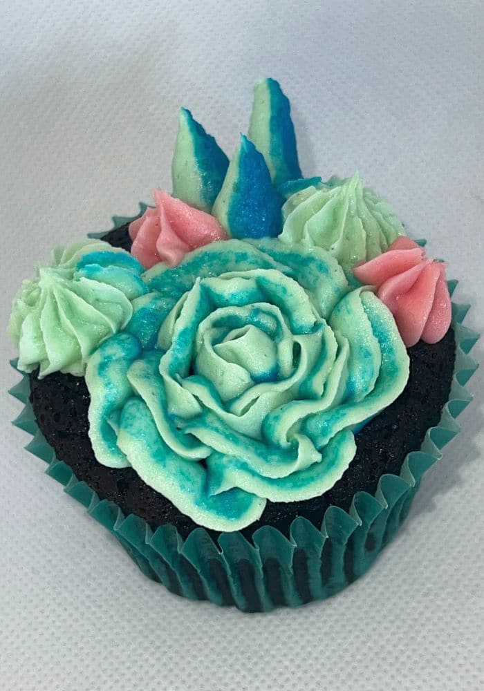 Cupcake piped with a teal buttercream rose surrounded by small succulents