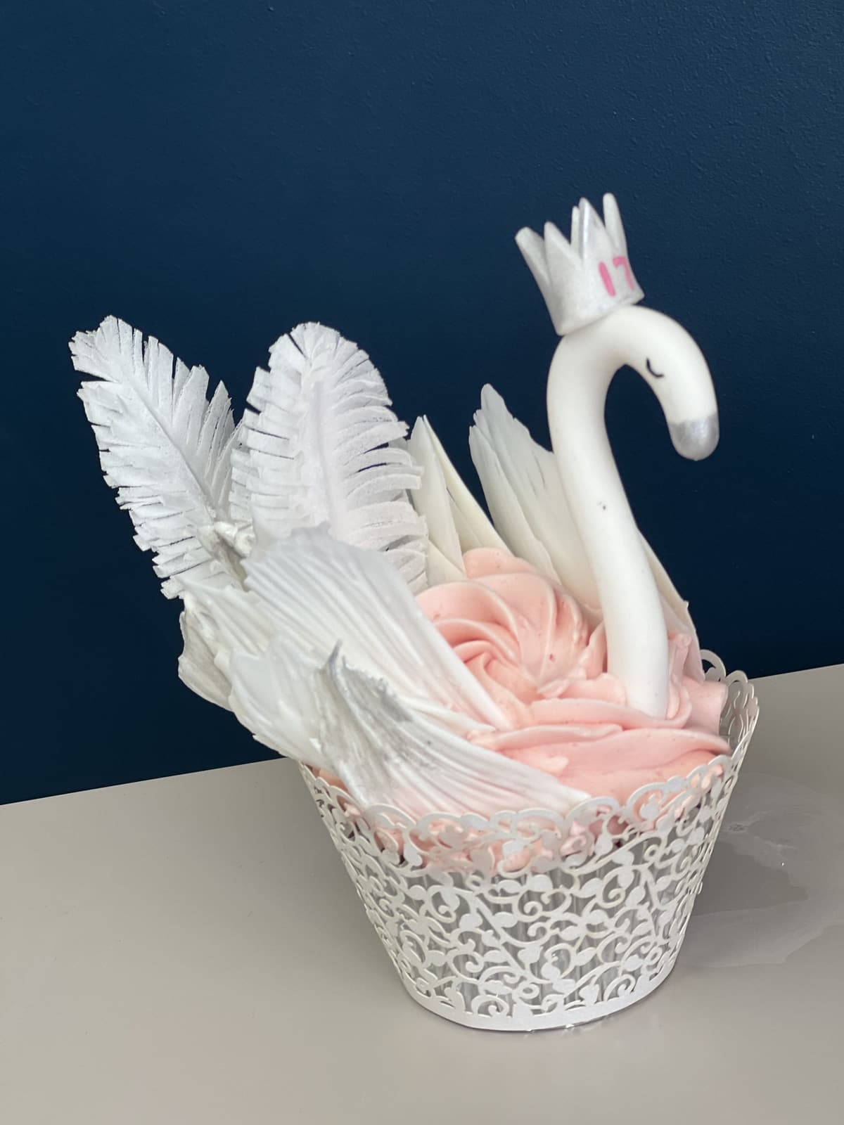 Cupcake piped as a white swan with feathered wings and blush frosting