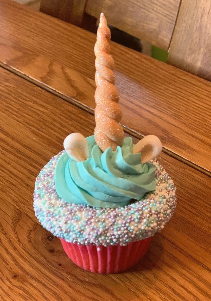 Unicorn cupcake with teal frosting, a sugar horn and rainbow sprinkles