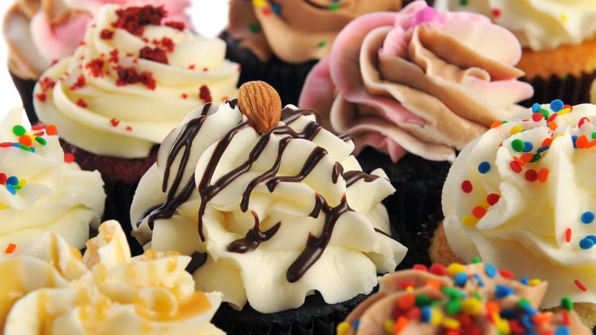 Close-up of cupcakes with piped cream frosting, chocolate drizzle and an almond