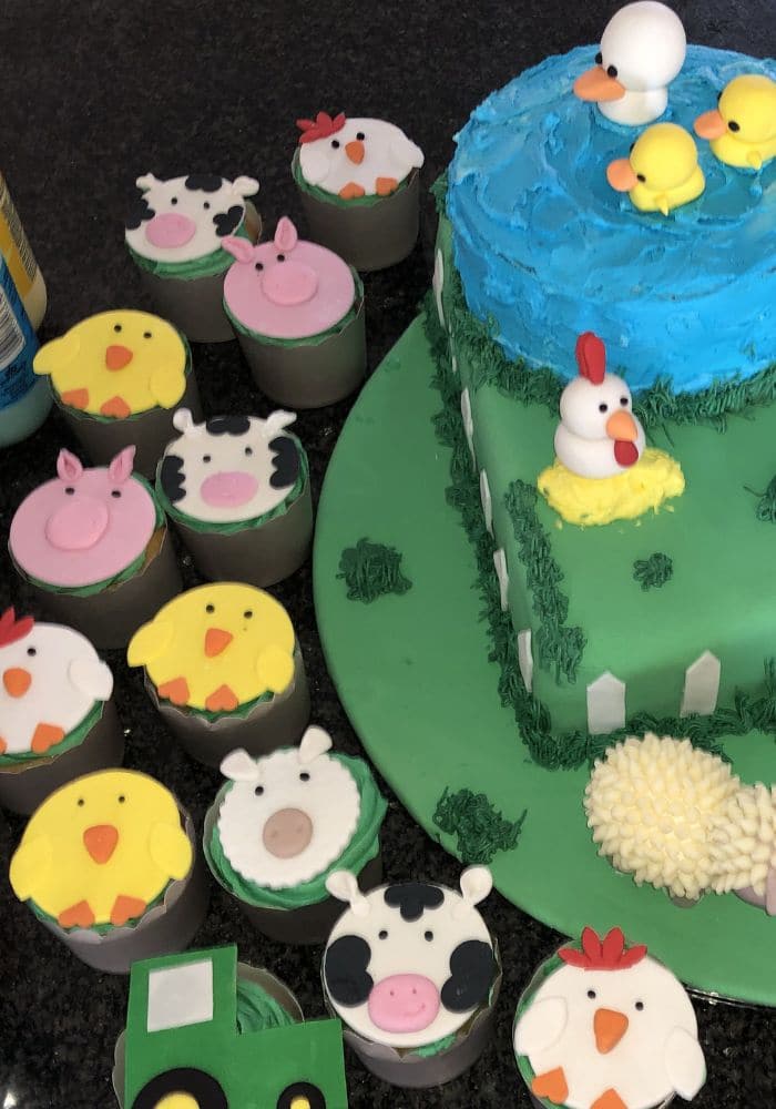 Cupcakes decorated as cows, chicks and pigs beside a farmyard cake