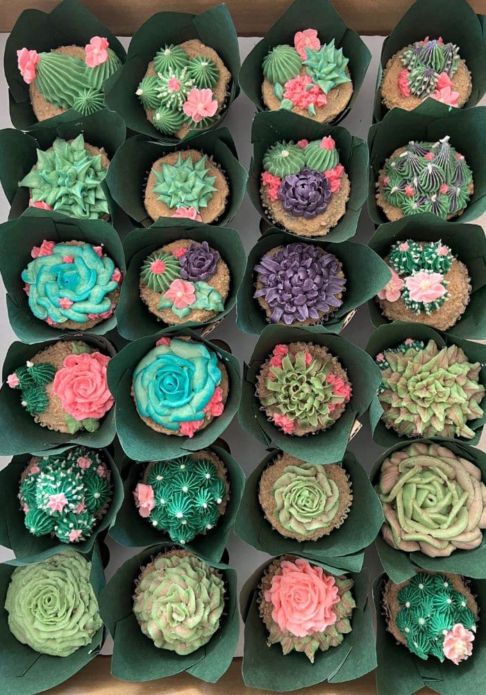 A tray of cupcakes piped as succulents and cacti in greens, teals and pinks