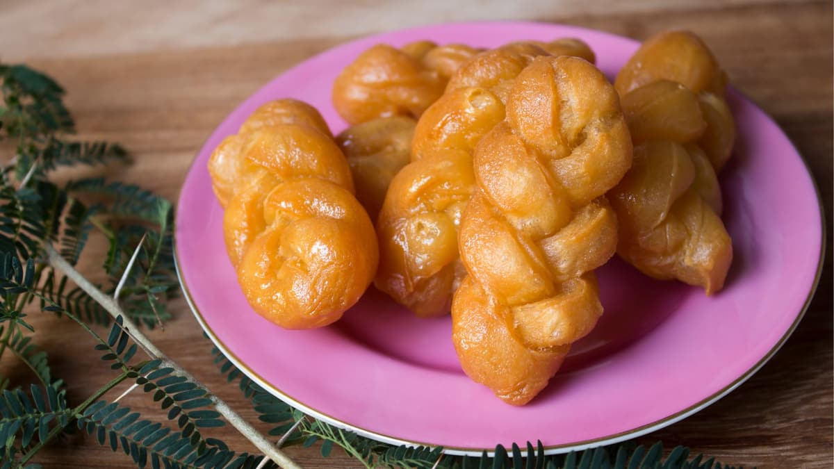 Golden plaited koeksisters, glossy with syrup, on a pink plate
